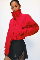 Chaqueta corta roja ZARA Woman Collection con mezcla de algodón, cuello alto, manga larga, bolsillos delanteros y cinturón ajustable con lazada en el mismo tejido. Cuenta con cierre frontal con botones ocultos por solapa.