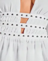 Top blanco con escote halter y espalda descubierta, confeccionado en microtul con detalle de tachas en la cintura.