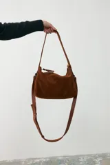 Cartera mediana de gamuza color tostado con detalles en cuero liso al tono. Cuenta con doble asa fija para llevar al hombro y una correa larga desmontable y regulable para usar como bandolera. Posee cierre superior.