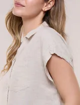 Camisa de lino de estructura recta, color beige con rayas verticales blancas. Cuenta con cuello solapa, escote en V abierto, abotonadura frontal, bolsillo plaqué en el pecho, mangas cortas de hombro caído y ruedo recto.