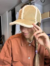 Gorro tipo béisbol color beige con borde de piel sintética blanca.