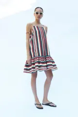 Vestido mini confeccionado en hilatura con lino, de escote recto con tirantes finos ajustables y bajo acabado con volantes, con diseño de rayas verticales en la parte superior y horizontales en el volante.