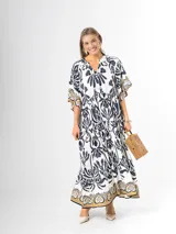 Maxi vestido blanco con estampado paisley en azul marino y detalles en tonos dorados, con cuello en V, mangas amplias y diseño escalonado.