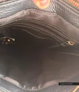 Cartera negra de cuero convertible en mochila, con tapa superior, cierre metálico, terminaciones trenzadas, forro de gabardina de algodón, bolsillos internos y externos con cierre.