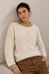 Sweater de tejido de punto artesanal color marfil, con diseño de rombos en relieve, cuello redondo, puños y dobladillo en tono marrón tostado.