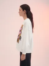 Buzo blanco de corte clásico con estampa rectangular centrada en el frente con flores rosadas y texto en color ocre.