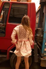 Camisa larga de brocato con diseño de flores, escote en V y cierre frontal con lazos ajustables. Presenta mangas largas con cordones entrelazados y detalles de flecos en los puños y el ruedo.