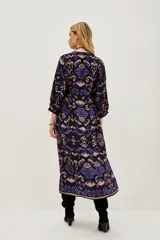 Vestido midi de viscosa con estampado estilo ikat en tonos oscuros, violetas y azules. Presenta mangas largas, cuello redondo y un diseño holgado que se ajusta a la cintura mediante un cinturón.