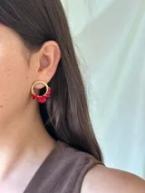 Aro de metal dorado de 2 cm de diámetro, con cuentas de vidrio facetadas de color rojo colgando en la parte inferior.