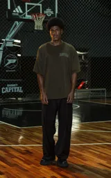 Remera de manga corta y cuello redondo, calce oversize, color marrón oscuro con efecto batik artesanal. Presenta un estampado frontal con la palabra "RAVERS" en tipografía universitaria con borde blanco.