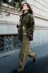 Chaqueta de algodón encerado con diseño de cuadros en tonos verde oliva, beige y líneas rojas. Presenta cuello solapa, cierre frontal con botones a presión metálicos, bolsillos de plastrón con solapa y un detalle de pañuelo desmontable sobre los hombros.