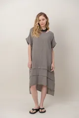 Vestido midi de lino color beige, de corte holgado y silueta acampanada. Cuenta con cuello redondo, mangas cortas amplias, bolsillos laterales y detalles de recortes horizontales en la falda con terminación asimétrica más larga en la parte trasera.