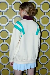 Buzo color crema con cuello alto y cierre frontal parcial. Presenta bloques de color en turquesa y bordó en los hombros y mangas, y un estampado frontal con la frase "SLOW WEEKEND SPORTY MOOD" en bordó.