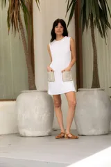 Vestido corto tejido en hilado de algodón en punto dolor, color blanco, con cuello redondo y sin mangas. Presenta dos bolsillos de lino aplicados en el frente.