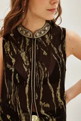 Camisa sin mangas, larga y abierta, con cuello alto y cierre frontal. Presenta un estampado abstracto en tonos marrón oscuro y dorado metalizado.