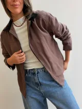 Campera de gabardina color beige con cierre frontal y cuello en contraste color negro. Presenta un diseño minimalista con bolsillos delanteros funcionales y calce cómodo.