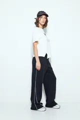 Pantalón babucha negro de silueta amplia y caída relajada, con detalle de líneas blancas laterales y cintura elastizada.