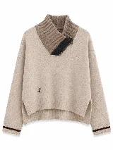 Polera tejida en lambswool color beige, con cuello alto acanalado y cierre frontal parcial. Presenta diseño de rombos en las mangas, puños con detalle de rayas en contraste y ruedo asimétrico con aberturas laterales.