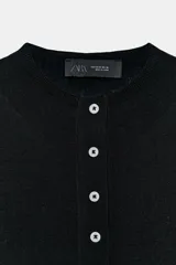 Chaqueta de punto fino color negro, con cuello redondo, manga corta y cierre frontal con múltiples botones a contratono.
