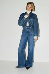 Jean de tiro alto con corte acampanado desde la rodilla. Presenta bolsillos tipo parche en la parte frontal y cierre con botón metálico.