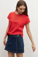 Remera de manga corta color rojo vibrante, con cuello redondo y un panel frontal con bordados calados (ojales) en forma de V invertida.