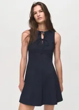 Vestido corto sin mangas de efecto denim en color azul marino, con cuello redondo y tirantes anchos. Presenta detalles de lazos en la parte delantera y diseño de tablas en la falda.
