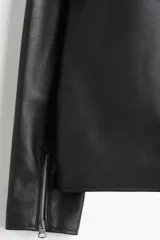 Campera negra de efecto cuero con cuello camisero, cierre frontal y bolsillos laterales con cierre. Presenta un corte estándar y forro interior.