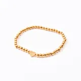 Pulsera elástica dorada con cuentas redondas y un dije de corazón.