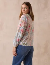 Blusa de gasa plisada con estampado floral en tonos rosas y celestes. Presenta cuello a la base con escote en V y lazo de ajuste frontal, mangas largas con puños elásticos y corte recto.