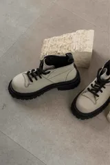 Botas de cuero color beige con suela track negra de goma y cordones gruesos negros. Presentan un diseño de caña baja con costuras visibles y puntera reforzada.