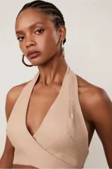 Top halter color beige confeccionado en lino, con escote en V cruzado, tiras medianas y lazada en el frente.