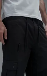 Pantalón cargo de corte oversize y silueta estructurada, confeccionado en microfibra pesada con leve elasticidad. Presenta cintura elástica con cordón de ajuste externo, cierre frontal con botón metálico, bolsillos laterales y bolsillos cargo de gran tamaño con tapa y broches a presión.