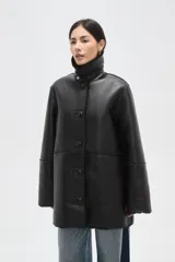 Tapado de eco-cuero negro con interior y cuello de piel sintética, cierre frontal con botones y diseño holgado.