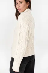 Campera beige de punto con diseño trenzado, cuello alto y cierre frontal.