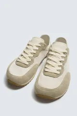 Zapatilla deportiva estilo barefoot, color marrón, con diseño de puntera ancha y redondeada. Confeccionada en una combinación de materiales textiles y detalles en serraje. Cuenta con suela fina de goma flexible y cordones en color crema.