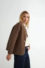 Campera corta de paño color negro, con cuello redondo, mangas largas y cierre frontal con botones a presión metálicos.