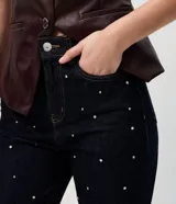 Pantalón de jean corte mom, color azul oscuro, con cintura alta y detalle de remaches metálicos distribuidos por toda la prenda. Cuenta con cierre frontal, botón y bolsillos funcionales.