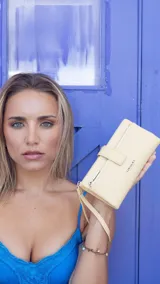 Billetera Lincoln's de tamaño mediano, color amarillo pastel, confeccionada en símil cuero. Cuenta con cierre frontal, solapa con broche, correa de mano tipo muñequera y logo de la marca grabado en el frente.