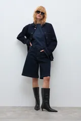 Bermuda de jean en color azul oscuro, con corte recto y largo hasta la rodilla. Presenta costuras a la vista en tono contrastante, cierre frontal con botón y bolsillos laterales.