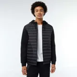 Buzo negro con capucha, cierre frontal con cremallera y mangas largas. El cuerpo es acolchado y las mangas son de tejido liso.