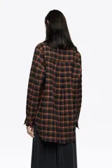 Camisa de corte recto y largo medio, confeccionada en tejido de algodón con textura. Presenta un diseño de cuadros en tonos rojo, negro y azul, cuello camisero, cierre frontal con botones, manga larga con puños abotonados y bolsillo de plastrón en el pecho.