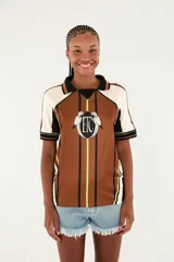 Camiseta deportiva estilo polo de color marrón con diseño estampado, cuello negro y detalles en blanco y verde flúor. Cuenta con mangas cortas y escudo frontal con las iniciales 'ETC' flanqueadas por aves.