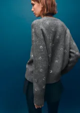 Sweater de punto fino color gris con cuello redondo, manga larga y diseño decorado con cristales brillantes distribuidos por toda la prenda.
