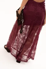 Vestido largo de encaje color bordó, con escote halter y diseño ajustado en el torso que se extiende hasta la cintura, donde continúa con una falda larga de encaje transparente.