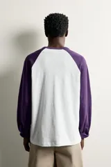 Remera manga larga de corte regular fit, con diseño estilo raglán en color blanco y mangas en color violeta oscuro.