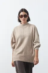 Polera de tejido de punto color gris, con cuello alto, mangas largas abullonadas con puños elásticos y costura central vertical en el frente. Presenta una abertura sutil en la espalda.