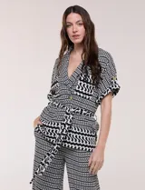 Conjunto de dos piezas de calce fluido y relajado con estampado geométrico en blanco y negro. Incluye una chaqueta con escote en V, solapa, diseño cruzado con lazo y bolsillos con solapa en el pecho, y un pantalón de tiro alto y corte wide leg.