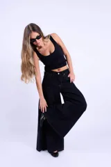 Jean de corte wide leg en color negro, con diseño de costuras curvas en la parte superior y pinzas que aportan volumen a la prenda. Presenta tiro medio, cierre frontal con botón y costuras en contraste.