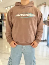 Hoodie boxy fit de color marrón topo, con capucha y diseño gráfico en el pecho con las palabras "Duxon Creative Studios" en blanco sobre un óvalo celeste.