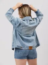 Campera de jean celeste con detalles de roturas, corte oversize, cuello clásico, cierre con botones metálicos, bolsillos frontales con solapa y puños abotonados.